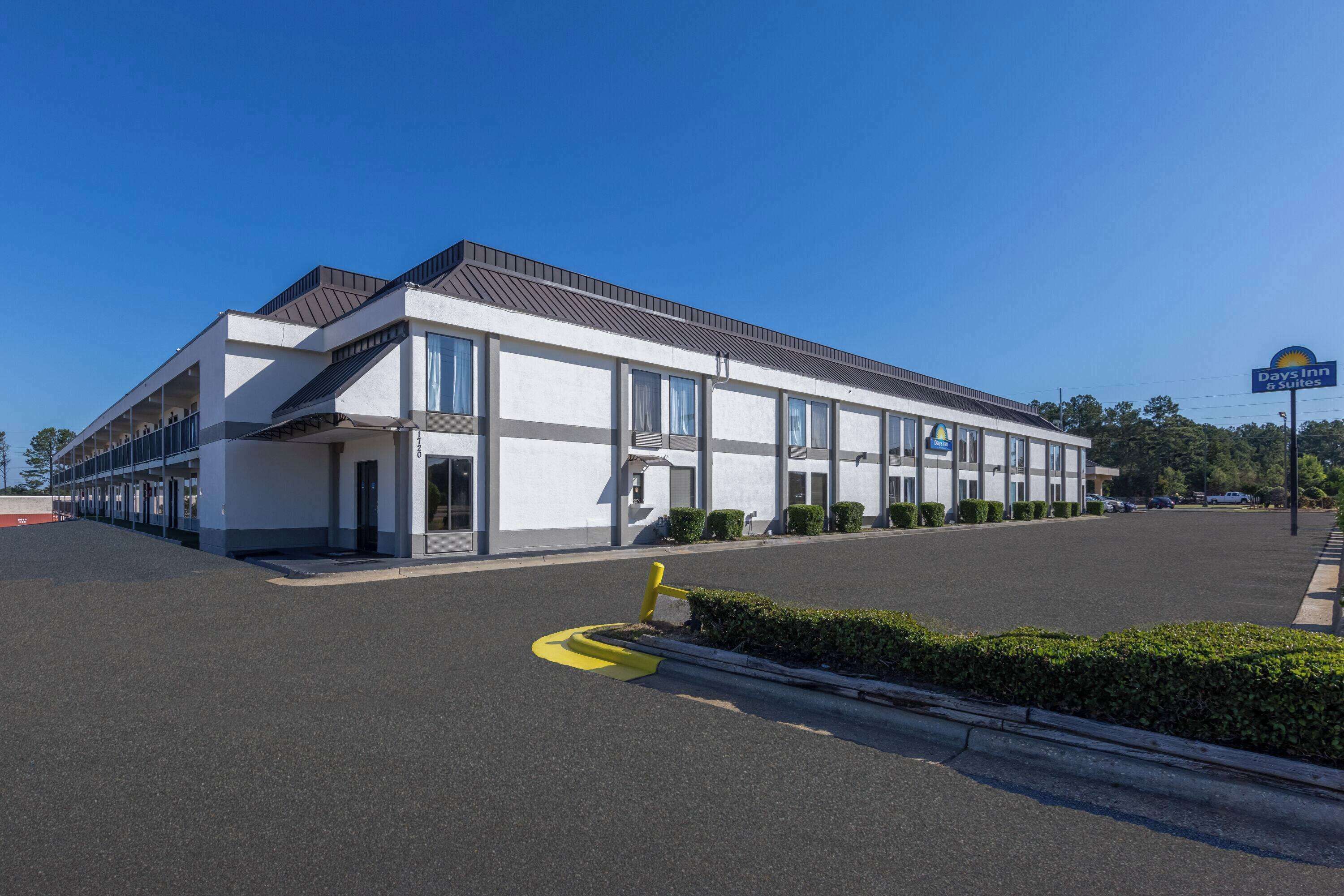 A modern hotel with a flat roof, large windows, and a parking lot.