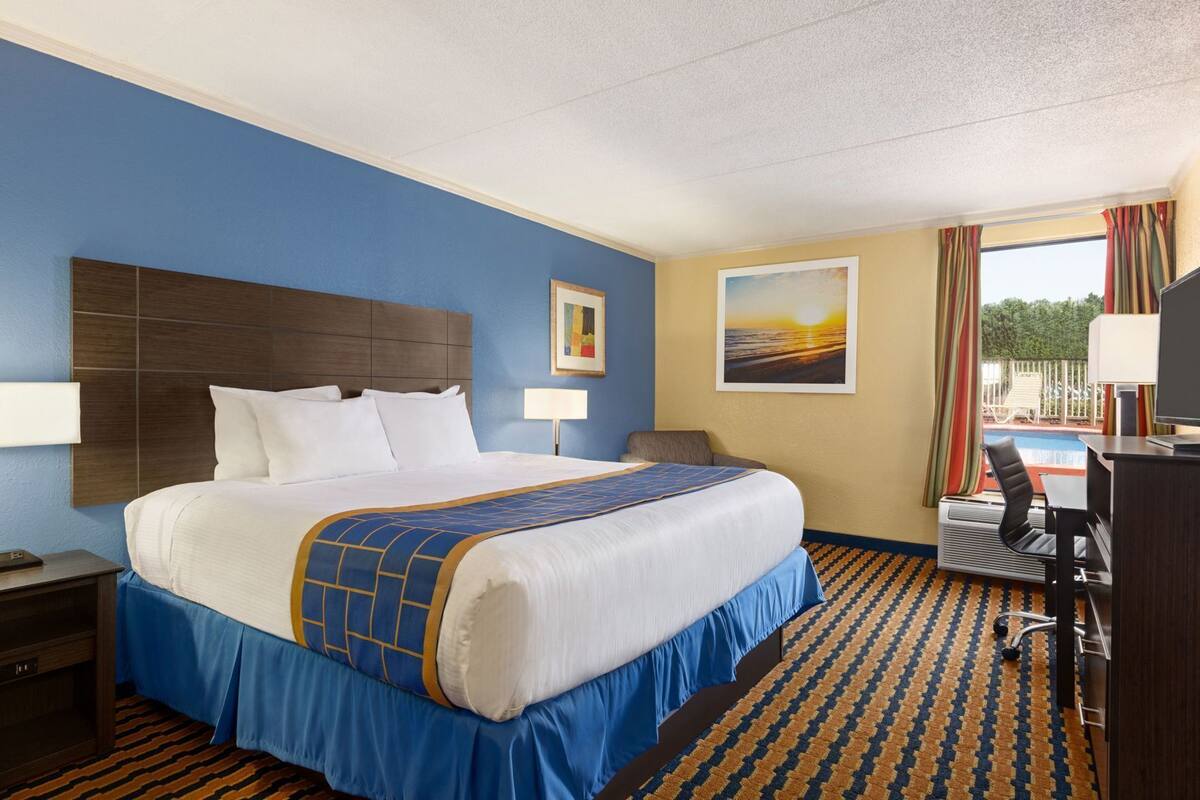 Une chambre d’hôtel avec un grand lit, un bureau, une chaise, une télévision et une vue sur l’extérieur.
