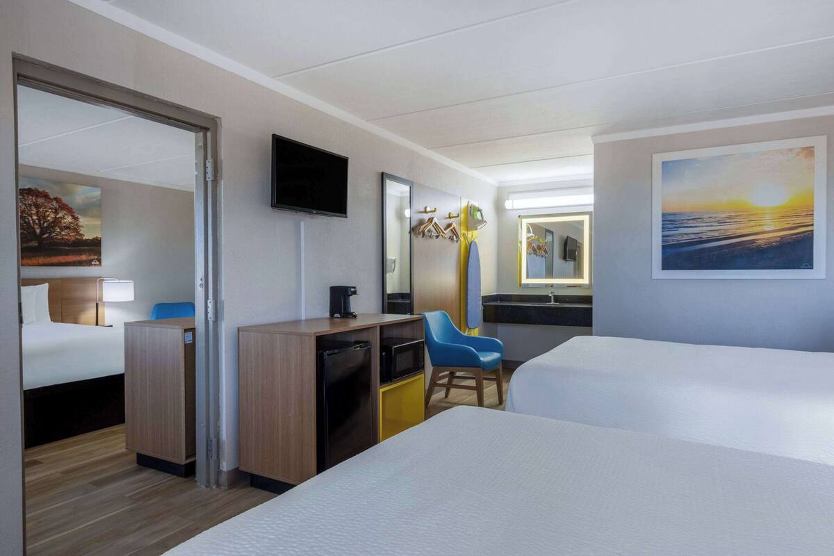 Une chambre d’hôtel avec deux lits, un bureau avec une chaise, une télévision et des œuvres d’art accrochées aux murs.