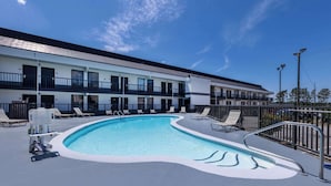 Ein Schwimmbecken mit Liegestühlen und ein Gebäude mit Balkonen im Hintergrund.