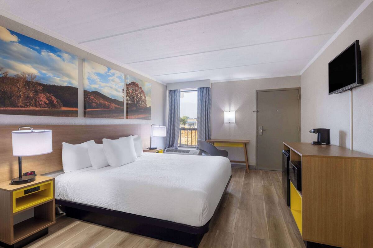 Une chambre d’hôtel avec un grand lit, un bureau, une télévision et un tableau représentant un paysage.