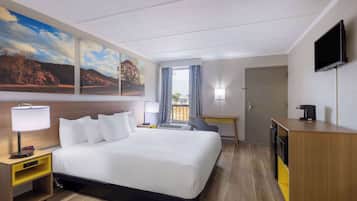 Ein Hotelzimmer mit einem großen Bett, einem Schreibtisch, einem Fernseher und einem Landschaftsbild.