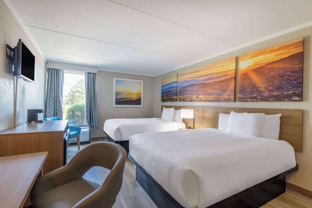 Une chambre d’hôtel avec deux lits, un bureau, une chaise et un téléviseur.