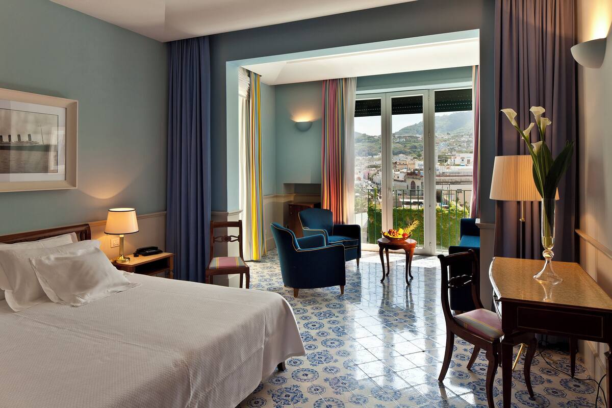 Une chambre d’hôtel avec un lit, un bureau, une chaise, une table et une vue sur la ville par la fenêtre.