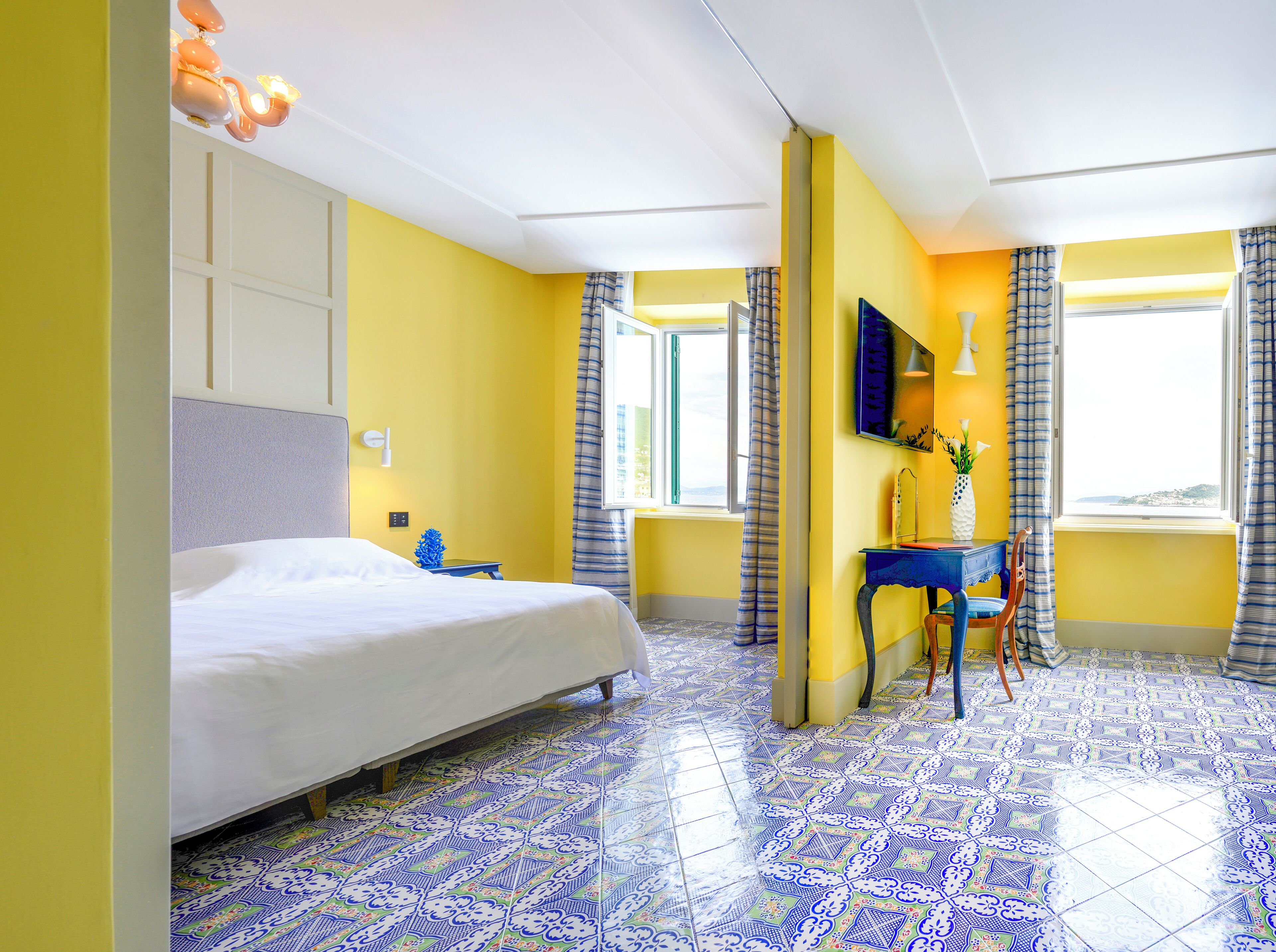 A hotel room with a bed, a desk, a chair, a TV, and a window with curtains.