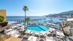A resort pool area with lounge chairs and umbrellas, a clear blue pool, and a marina with boats in the background.