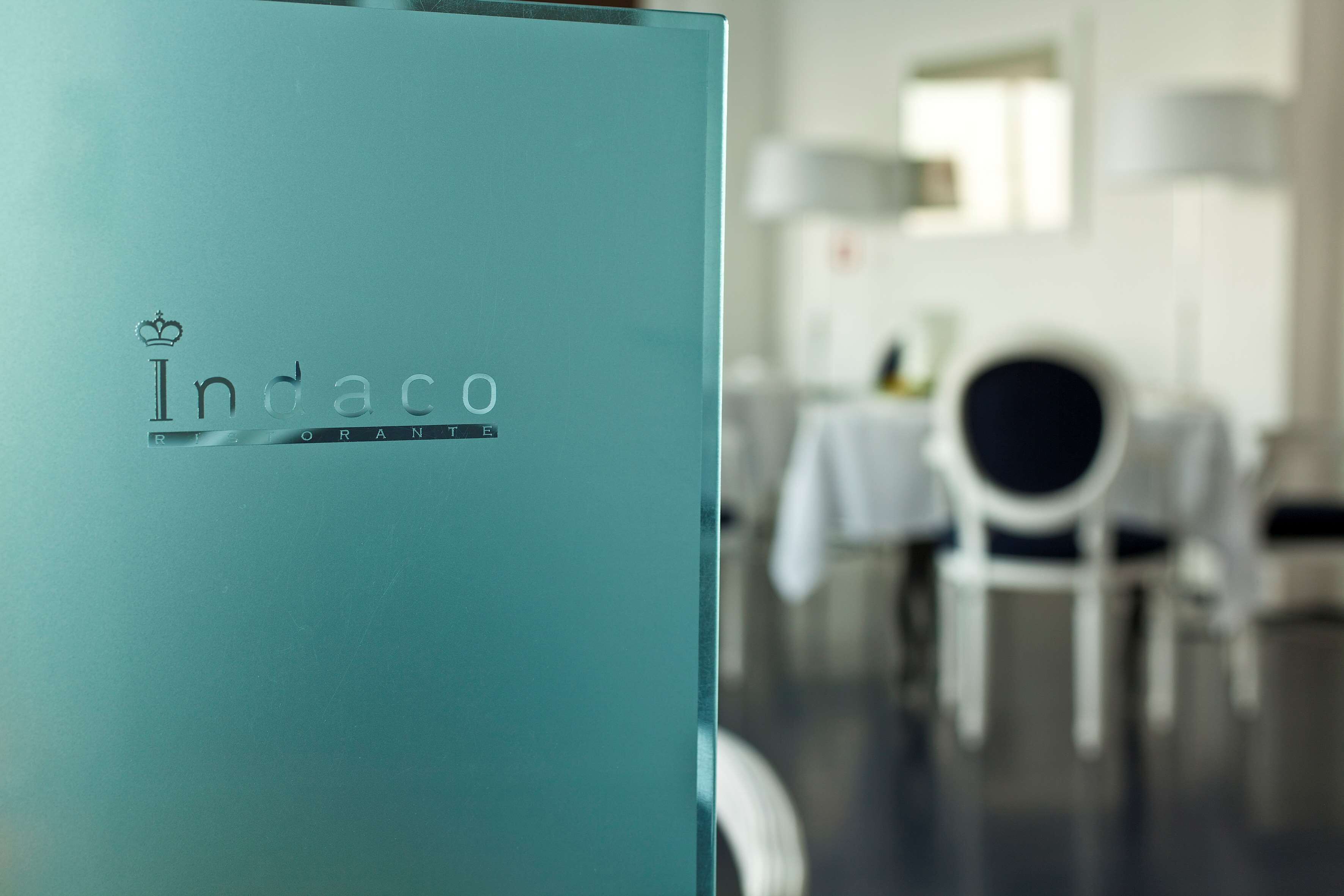 Un mostrador de recepción color turquesa con el logotipo “Indaco” y la palabra “RECEPTION” debajo.