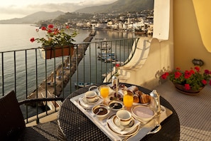 Un balcon avec un plateau de petit-déjeuner, une chaise et une vue sur une ville côtière et la mer.