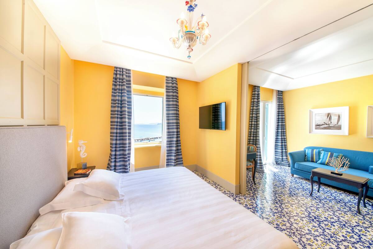 Une chambre d’hôtel avec un lit, un canapé, une télévision et vue sur la mer.
