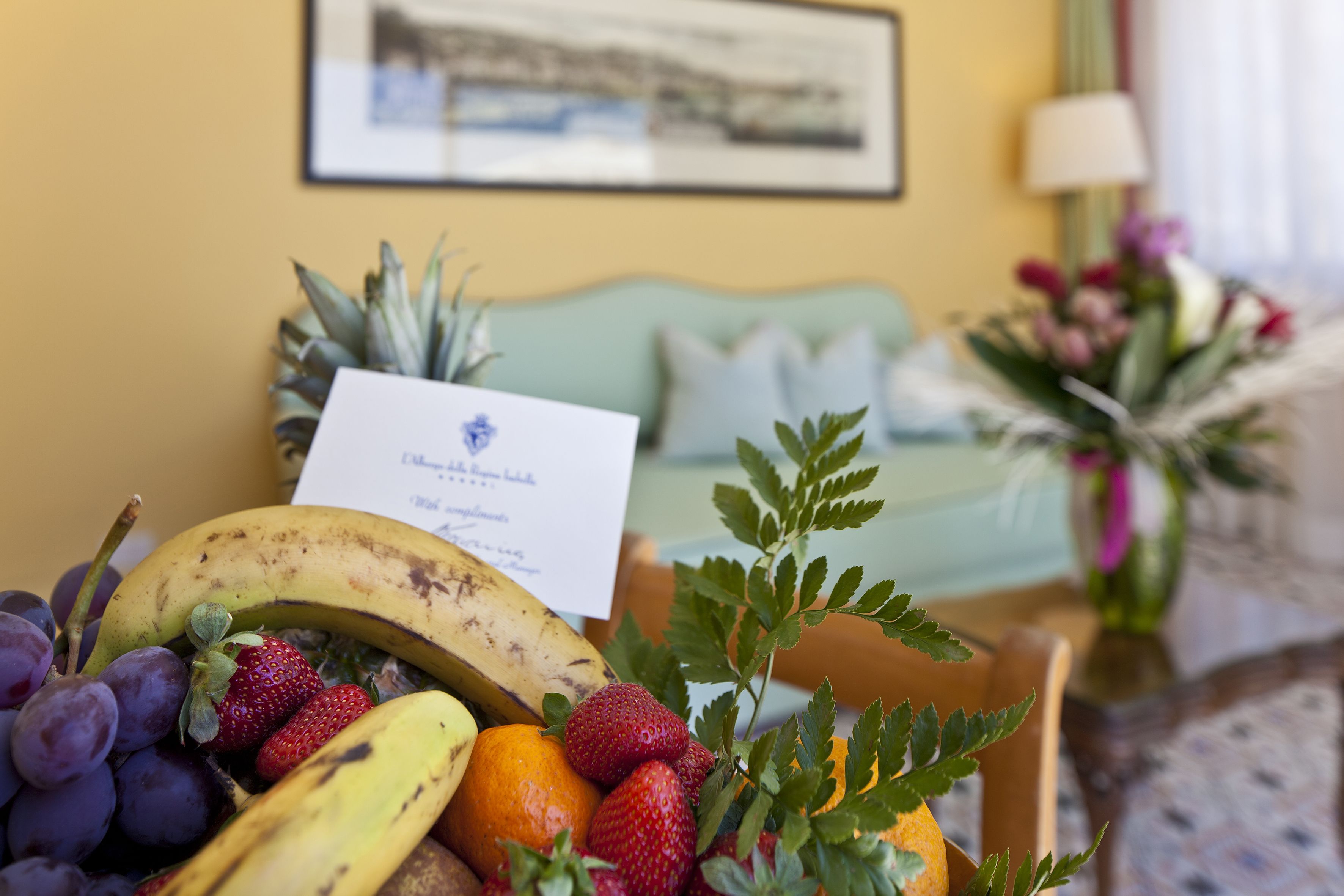 Uma cesta de frutas com uvas, morangos e uma banana em um quarto com um sofá verde claro e um quadro na parede.