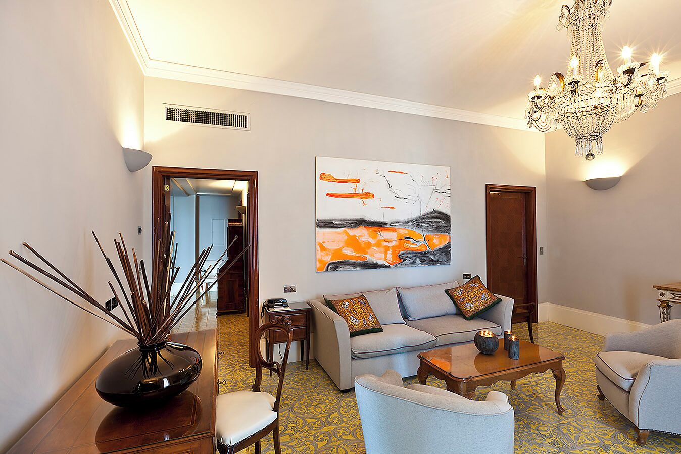 A living room with a sofa, armchairs, a coffee table, a chandelier, and a painting on the wall.