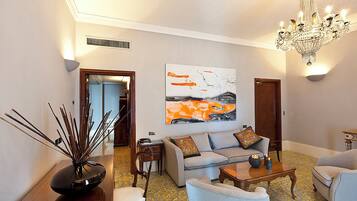 A living room with a sofa, armchairs, a coffee table, a chandelier, and a painting on the wall.