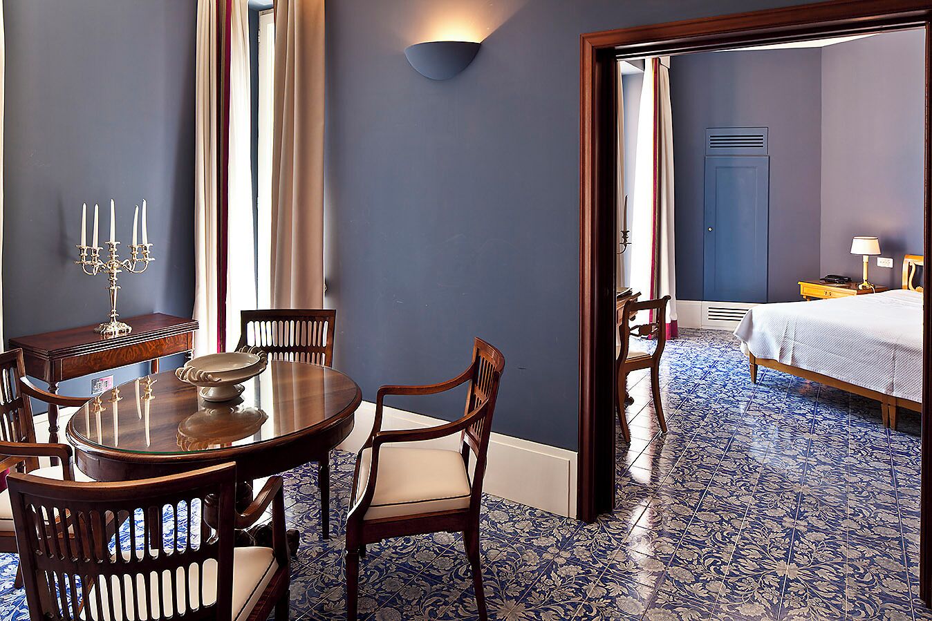 Une pièce comprenant une table à manger et des chaises, un lit avec un tapis à motifs bleus et blancs, et un luminaire fixé au mur.