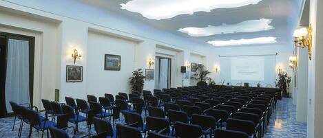 A conference room with rows of chairs, a projector screen, and wall-mounted lighting.