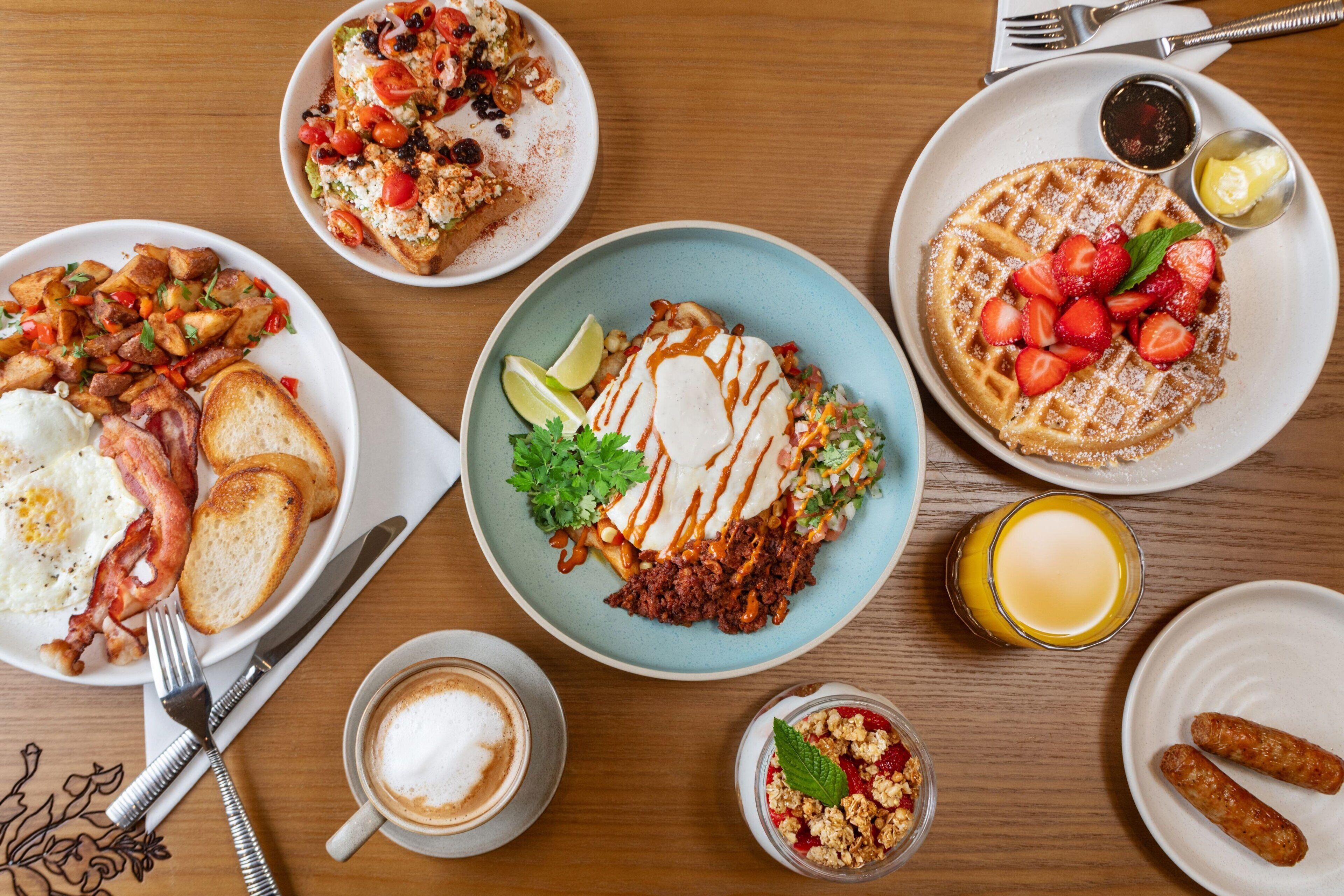 A breakfast table with various dishes including waffles, toast, eggs, and a cup of coffee.