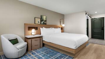 Una habitación de hotel con cama, una silla, una mesita de noche, una lámpara y una puerta.