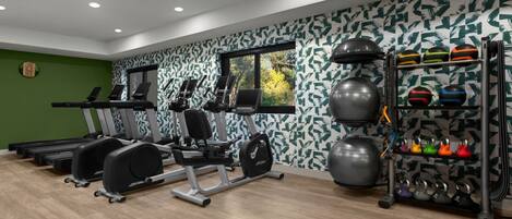 Une salle de sport moderne équipée de tapis de course, d’appareils de musculation et d’une variété de ballons d’exercice et d’haltères.