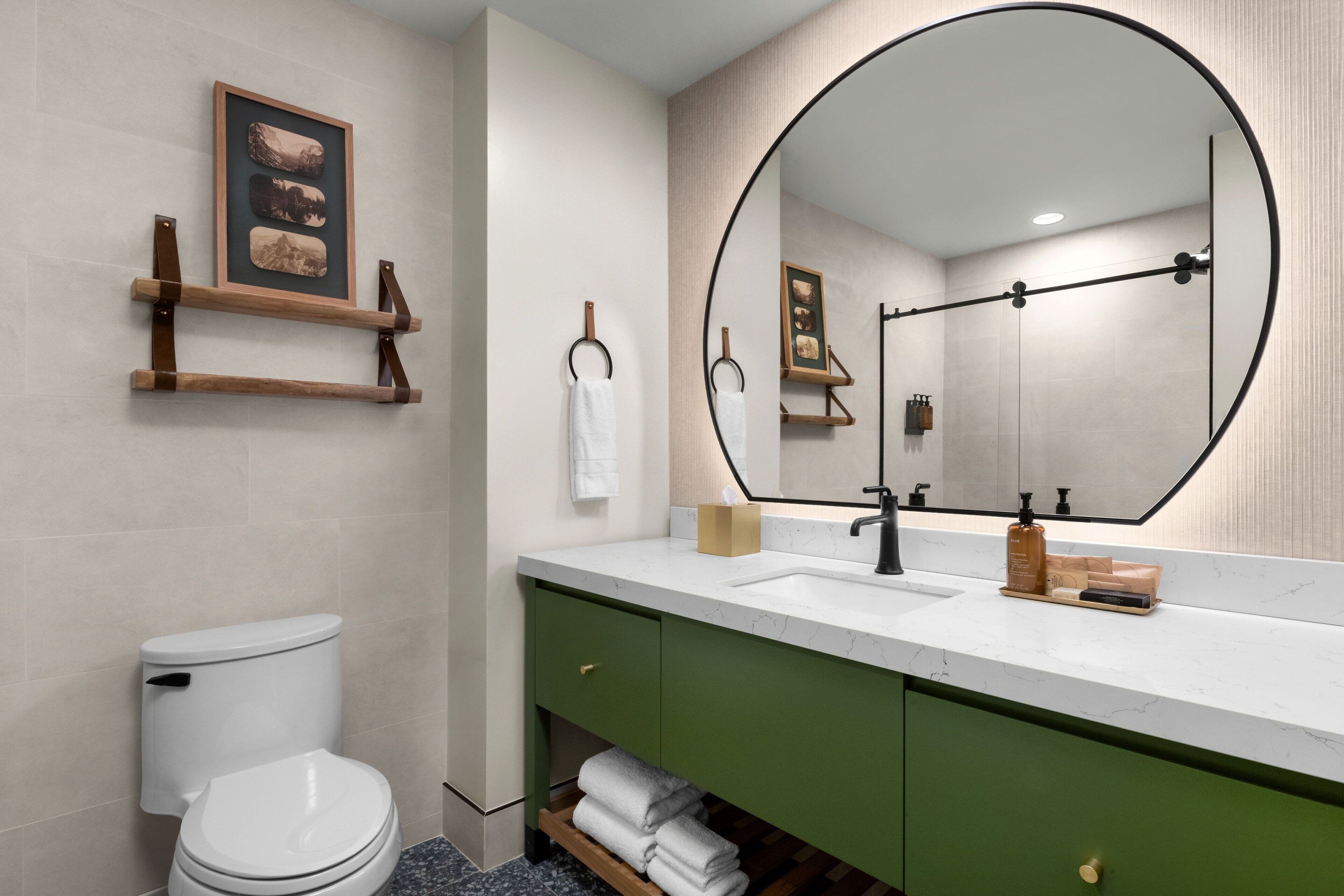 A modern bathroom with a white toilet, green vanity, and a large mirror with a black frame.