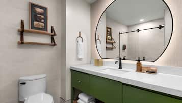 Un baño moderno con inodoro blanco, tocador verde y un espejo grande con marco negro.
