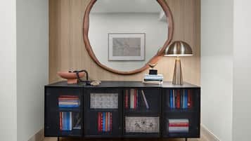Un interior moderno con un panel de madera, un espejo redondo grande, una consola negra con libros, un cuenco decorativo y una lámpara.