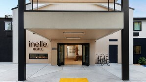 The entrance of Inelle Hotel with a clear pathway, a bike rack, and a visible interior through the open doors.