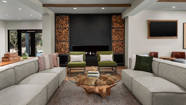 A modern living room with two green armchairs, a grey sofa, a glass coffee table, and a fireplace.