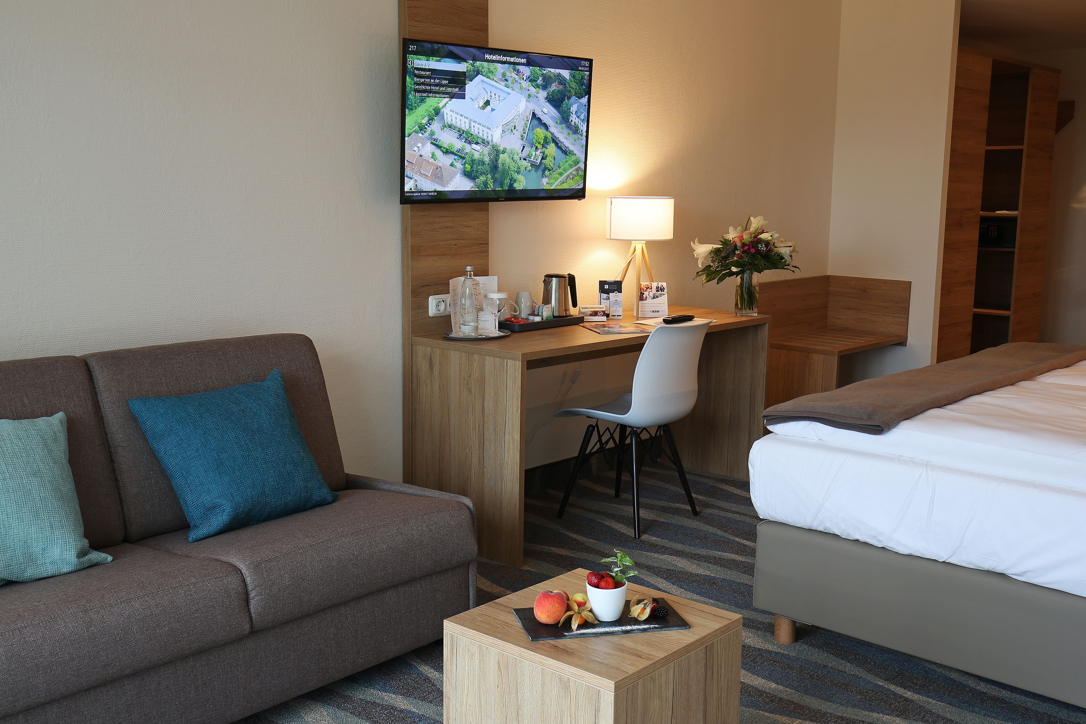 A hotel room with a sofa, a desk with a computer, a bed, and a small table with fruit.
