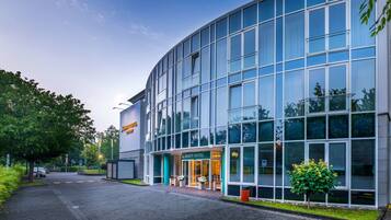 A modern hotel building with a glass facade, a sign for "Quality Hotel," and a well-maintained garden area.