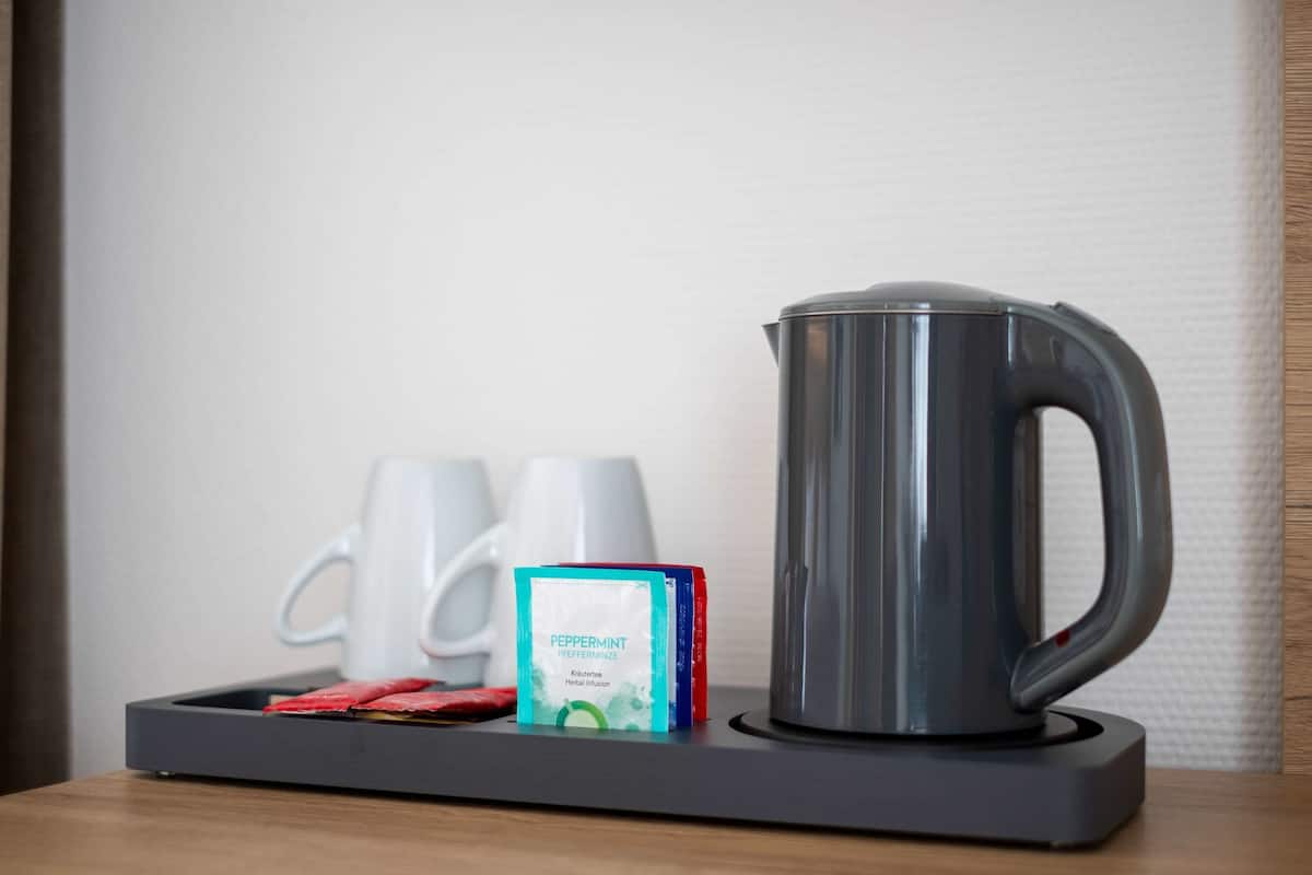A coffee maker, two white mugs, and a box of peppermint tea on a tray.