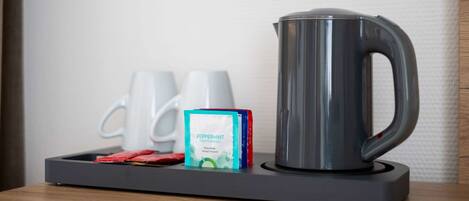 A coffee maker, two white mugs, and a box of peppermint tea on a tray.