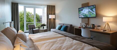 Habitación de hotel con una cama grande, un escritorio, un televisor y vistas al exterior.