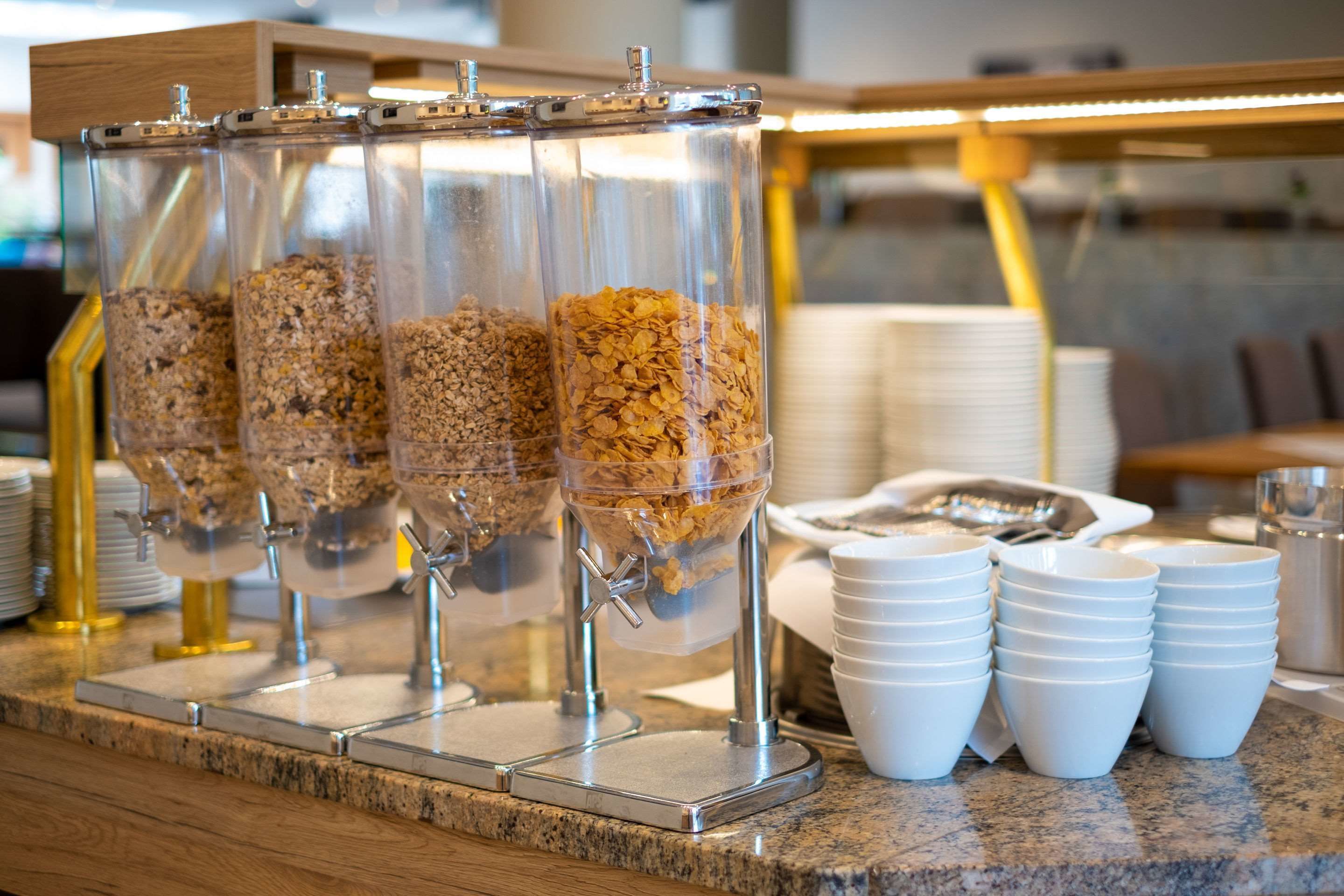 A breakfast bar with four dispensers filled with granola and cereal.