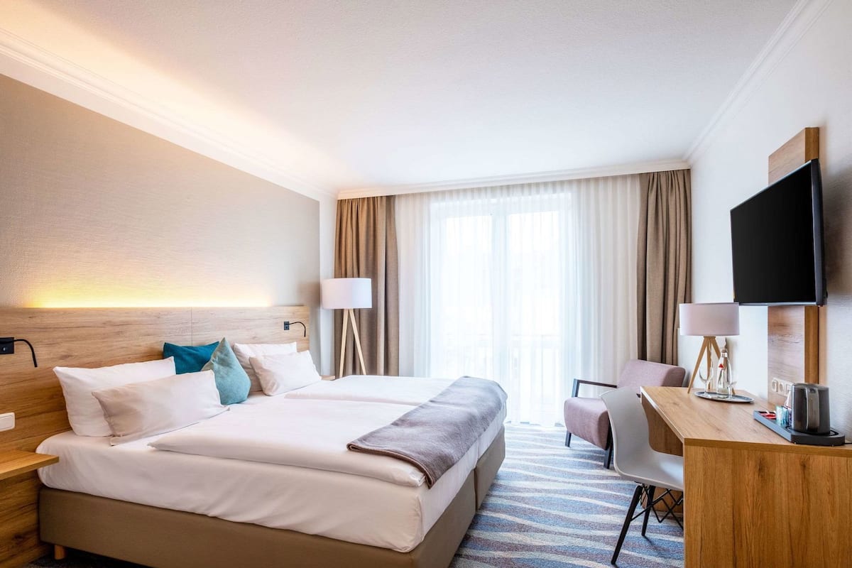 A hotel room with a large bed, a desk, a chair, a TV, and a window with curtains.