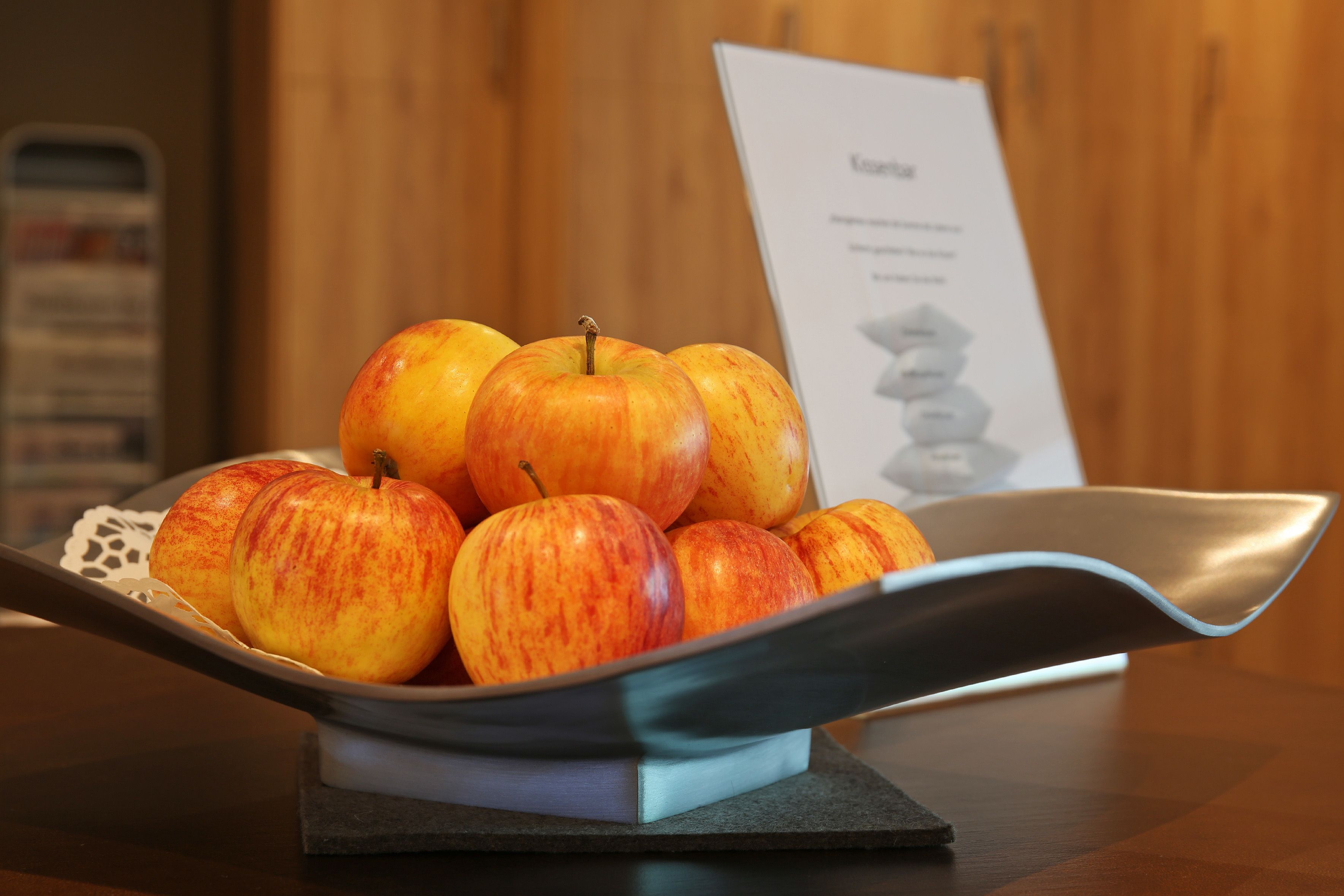 Un bol de manzanas sobre una mesa, con un mantel individual y un cartel de menú al fondo.