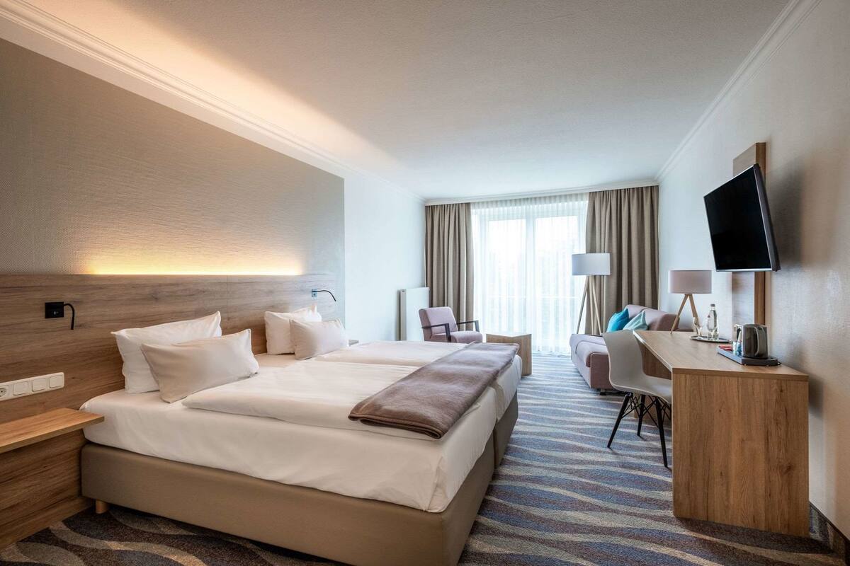 A hotel room with a large bed, a desk, a TV, and a window with curtains.