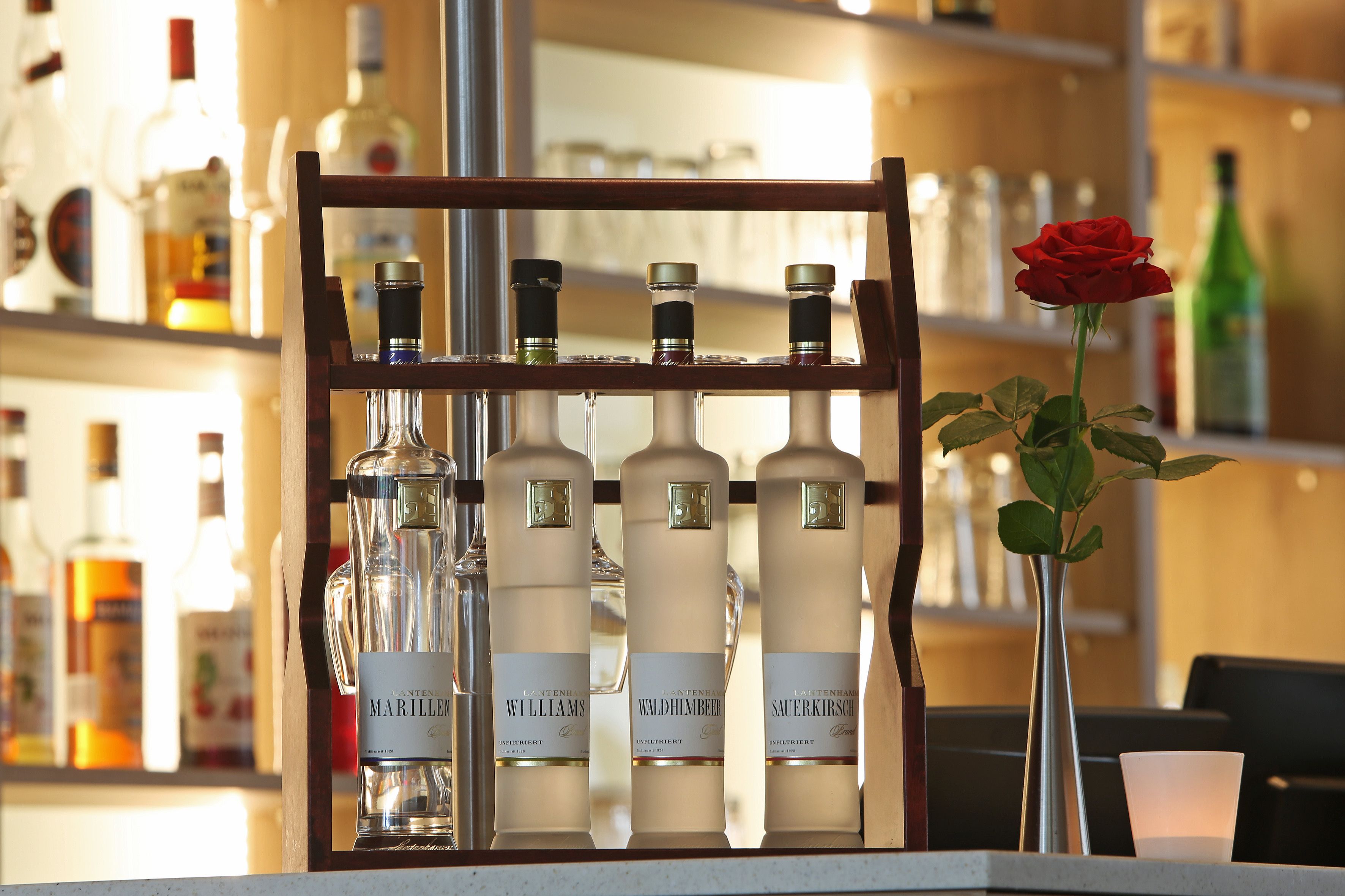 Eine Bar mit einer Auswahl an Spirituosenflaschen und einer roten Rose in einer Vase.