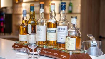 A selection of whiskey bottles on a bar counter with glasses and a wooden tray.