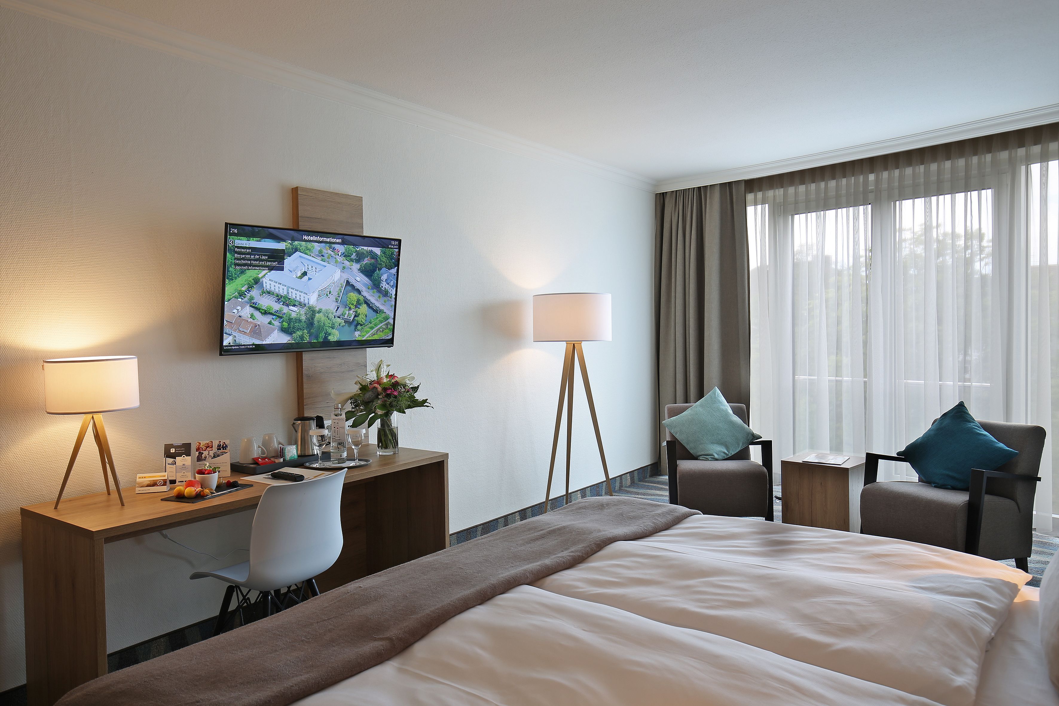 Habitación de hotel con una cama grande, un escritorio con computadora, un televisor montado en la pared y dos sillas.