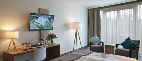 Habitación de hotel con una cama grande, un escritorio con computadora, un televisor montado en la pared y dos sillas.