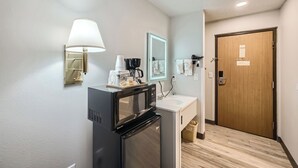 A compact hotel bathroom with a refrigerator, coffee maker, and a sink. - Travelodge by Wyndham Longmont (Longmont)