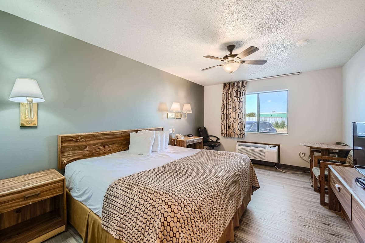 A hotel room with a bed, bedside tables, a desk, a chair, a ceiling fan, and a window with a view.