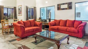 A living room with two red sofas, a glass-top coffee table, and a dining area with wooden chairs and a table. - Travelodge by Wyndham Longmont (Longmont)
