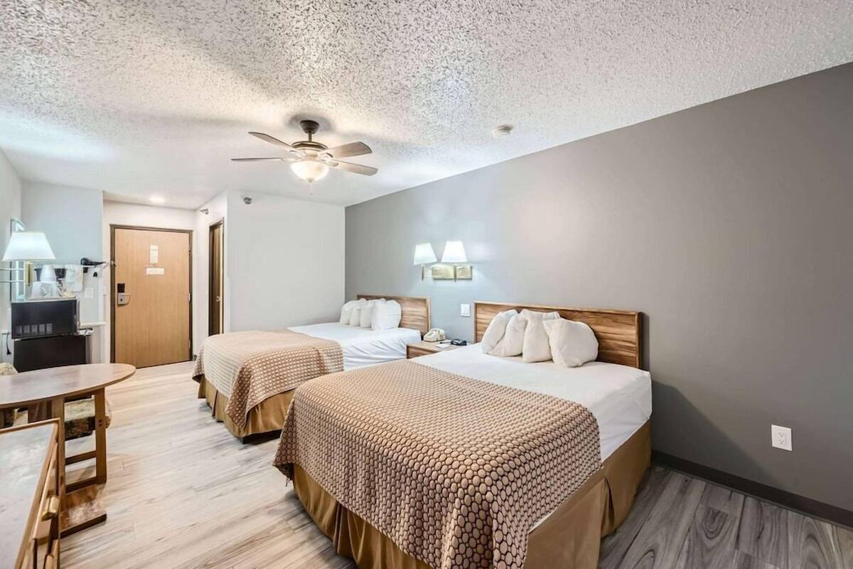 A hotel room with two beds, a desk, a chair, a ceiling fan, and a TV.