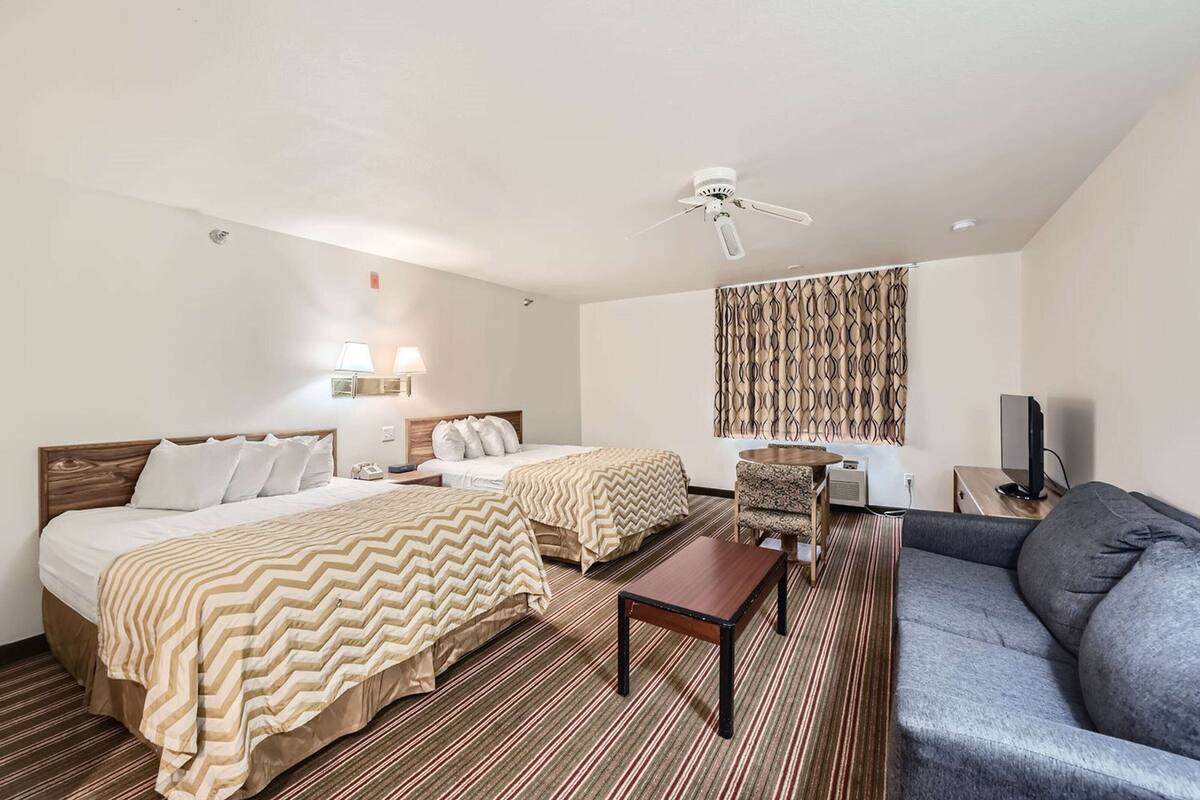 A hotel room with two beds, a sofa, a small table, a ceiling fan, a TV, and a patterned curtain.