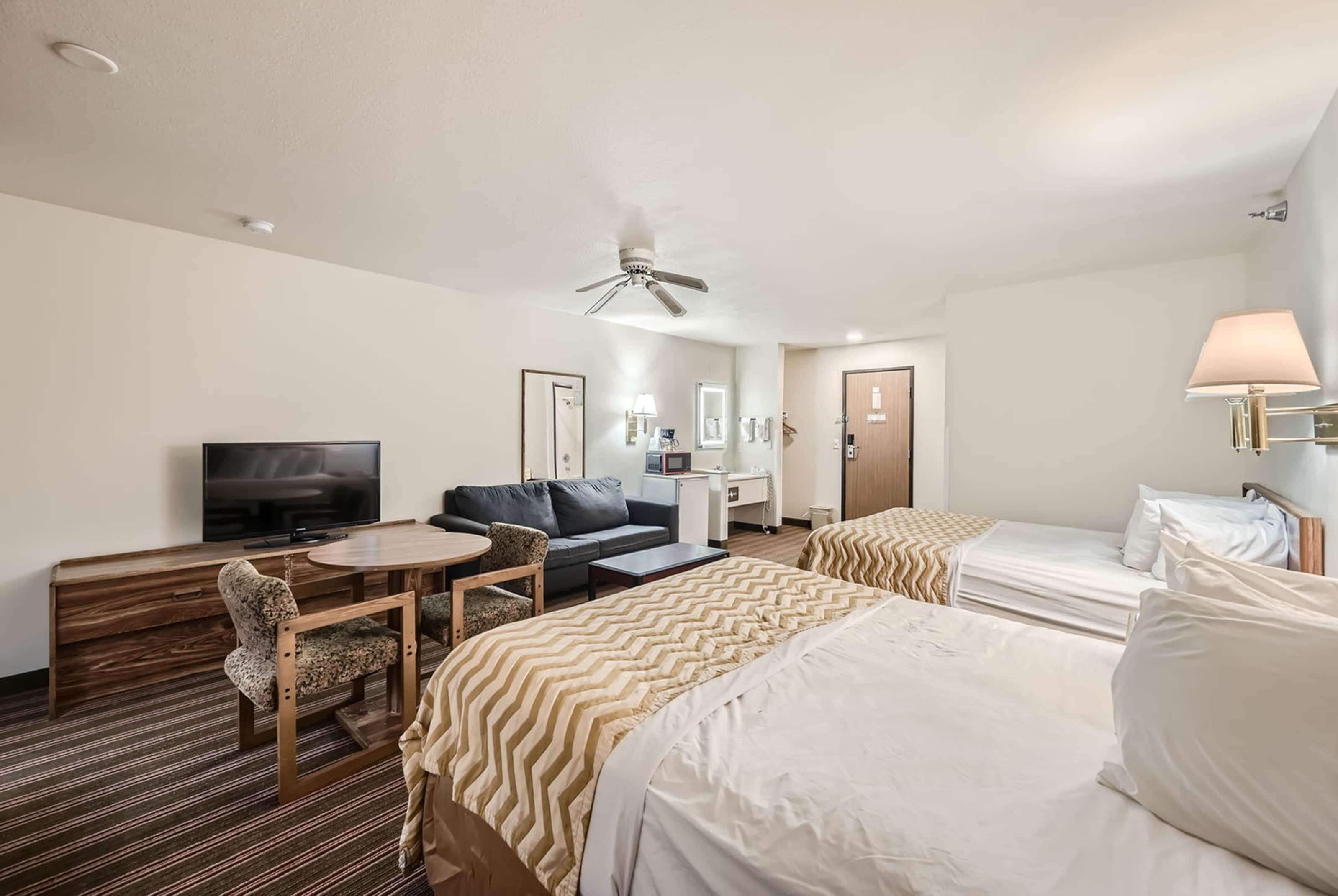 A hotel room with a bed, a sofa, a TV, a desk, and a ceiling fan.