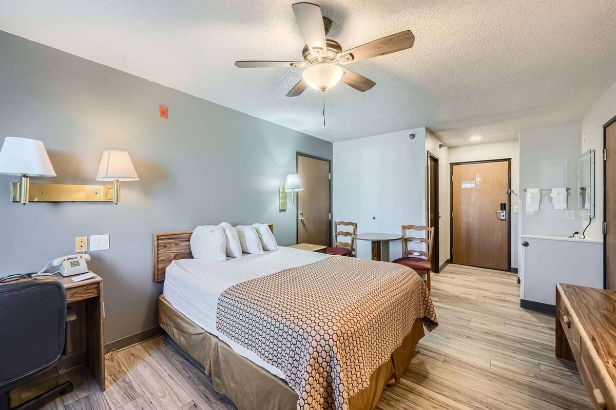 A hotel room with a bed, desk, chair, and a ceiling fan.