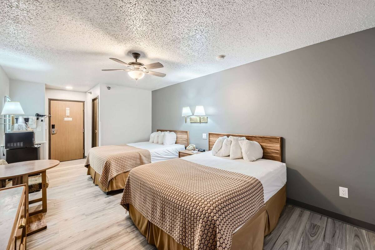 A hotel room with two beds, a desk, a ceiling fan, and a TV.