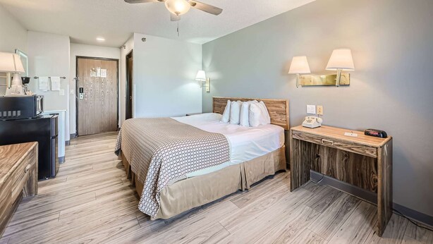 A hotel room with a bed, a desk, a ceiling fan, and a wall-mounted lamp. - Travelodge by Wyndham Longmont (Longmont)
