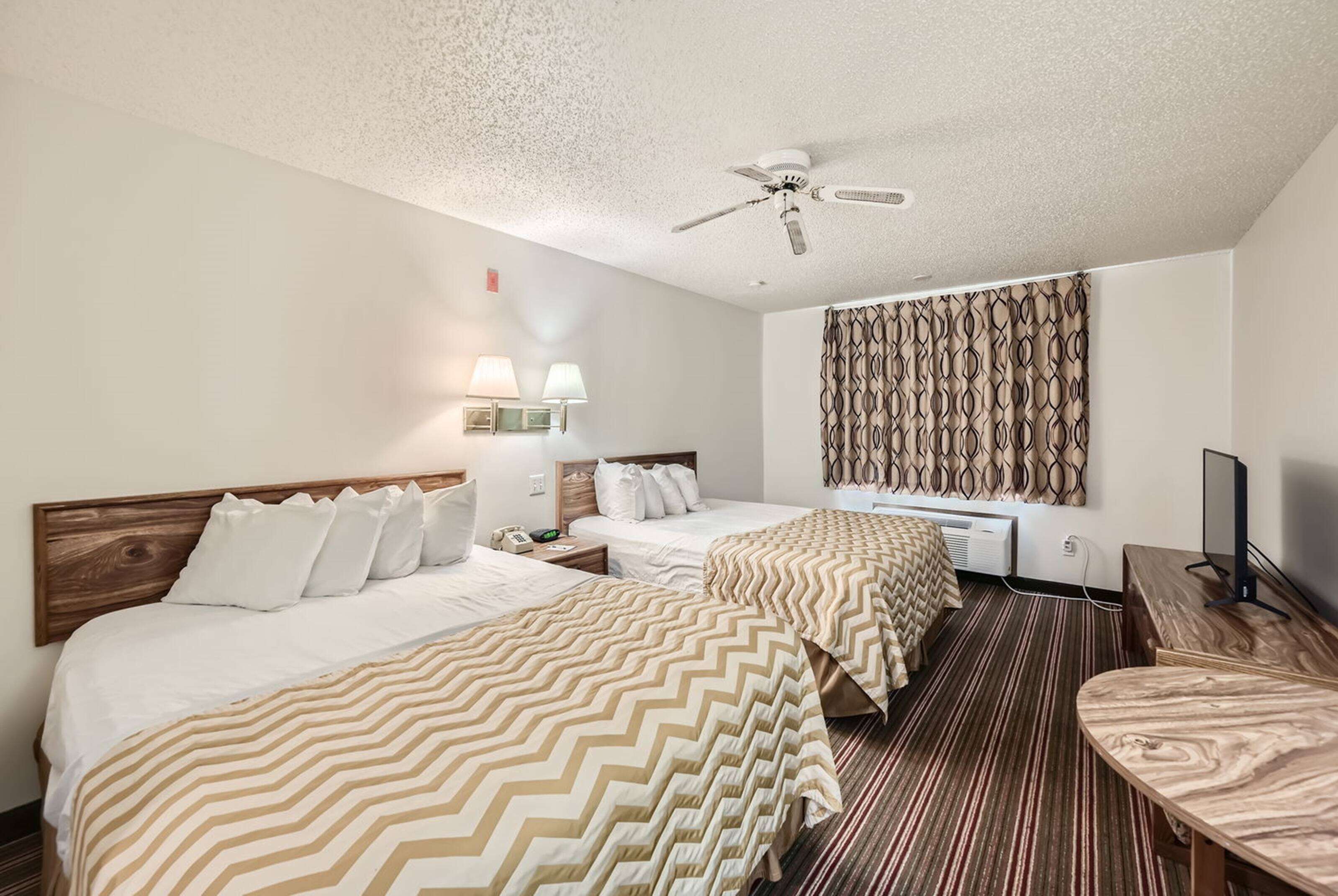 Une chambre d’hôtel avec deux lits, un ventilateur de plafond, un téléviseur fixé au mur et un rideau à motifs.