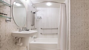 Un baño con bañera, lavamanos, ducha y estante de vidrio con artículos de aseo.